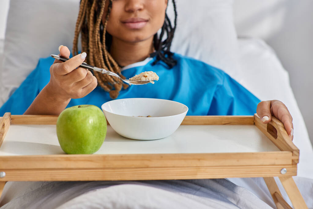 przycięty widok młodej afrykańskiej kobiety jedzącej śniadanie w szpitalnym łóżku, opieka zdrowotna - Zdjęcie, obraz