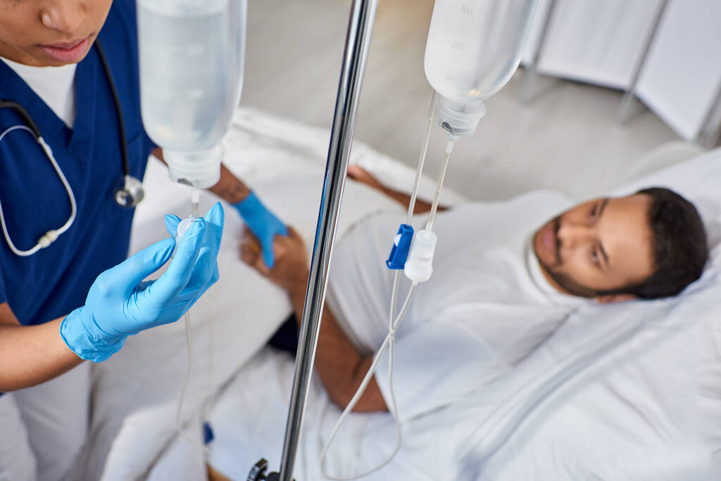 Сосредоточьтесь на африканской американской медсестре устанавливая счетчик рядом с размытым человеком, лежащим в больничной койке - Фото, изображение