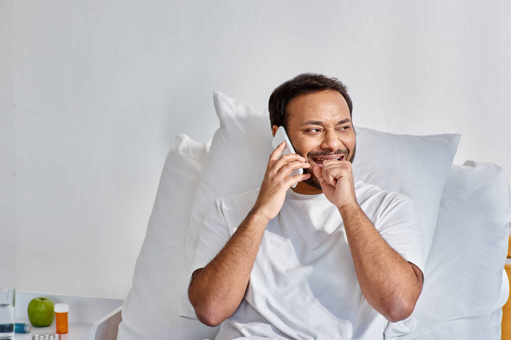 Hastane koğuşunda, sağlık hizmetlerinde yatarken neşeli, genç Hintli bir adam telefonla konuşuyor. - Fotoğraf, Görsel