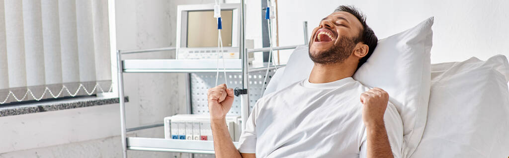 mladý šťastný indický pacient jásot a gesta aktivně zatímco v nemocniční posteli, zdravotní péče, banner - Fotografie, Obrázek