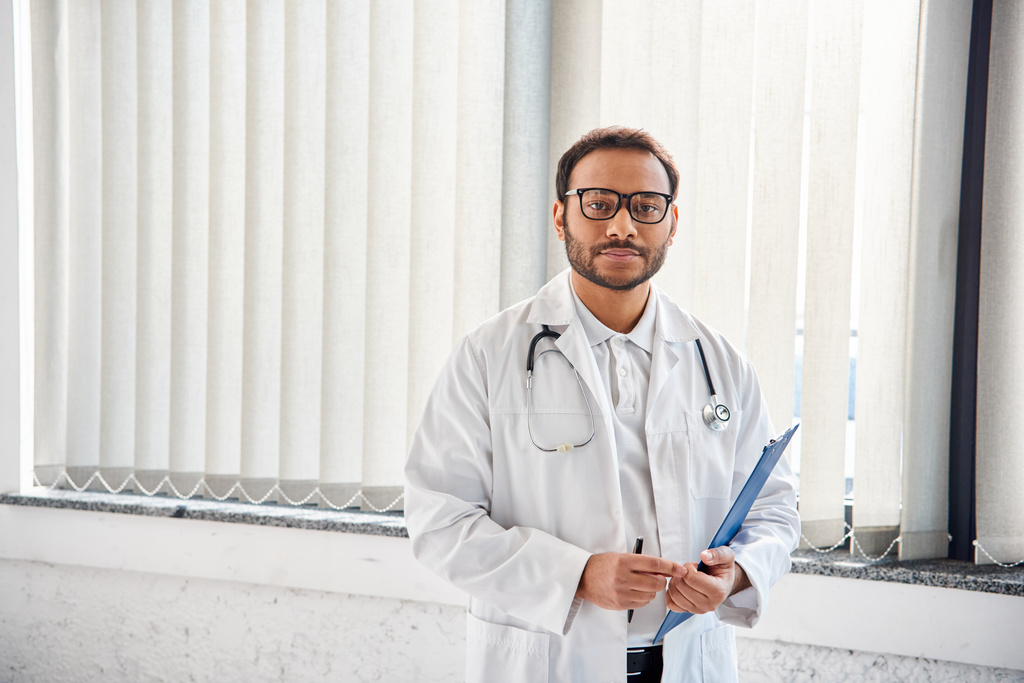 jonge Indiase arts met bril en stethoscoop in ziekenhuis afdeling kijken naar camera, gezondheidszorg - Foto, afbeelding