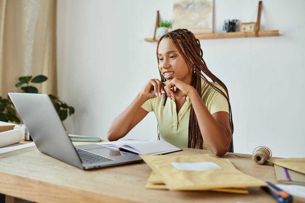 attraktive afrikanisch-amerikanische Verkäuferin schaut glücklich auf ihren Laptop, während sie hart arbeitet, Lieferung - Foto, Bild