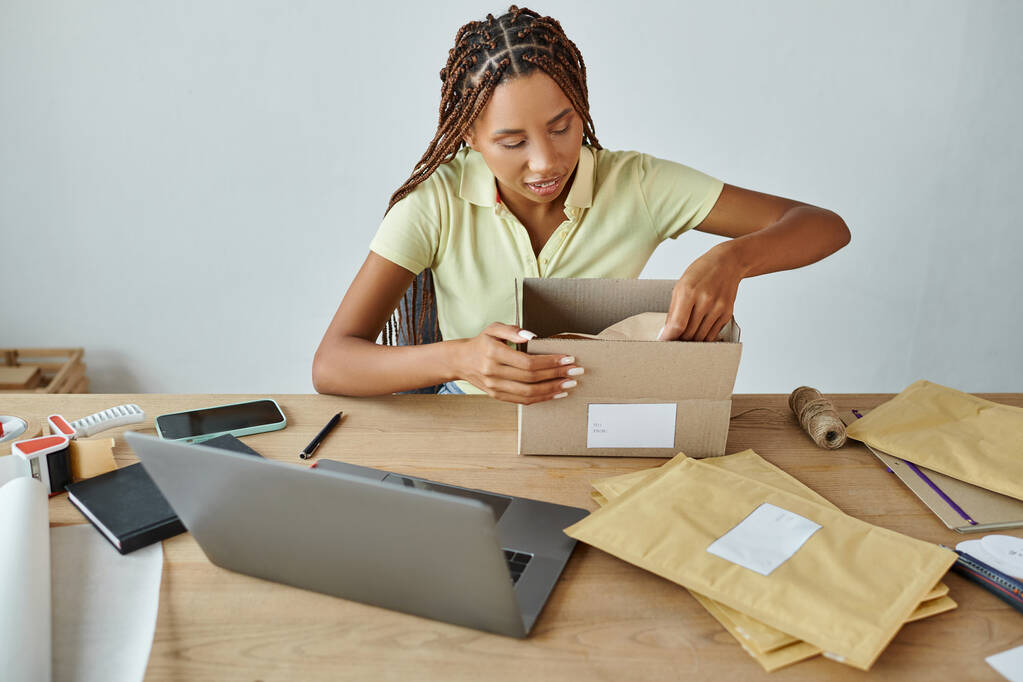 goed uitziende Afrikaanse Amerikaanse vrouwelijke retailer verpakking kartonnen doos aandachtig, levering concept - Foto, afbeelding
