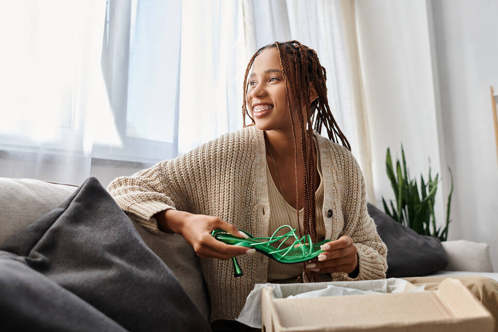 houkutteleva hilpeä afrikkalainen amerikkalainen nainen istuu sohvalla vihreät kengät käsissä ja katselee pois - Valokuva, kuva