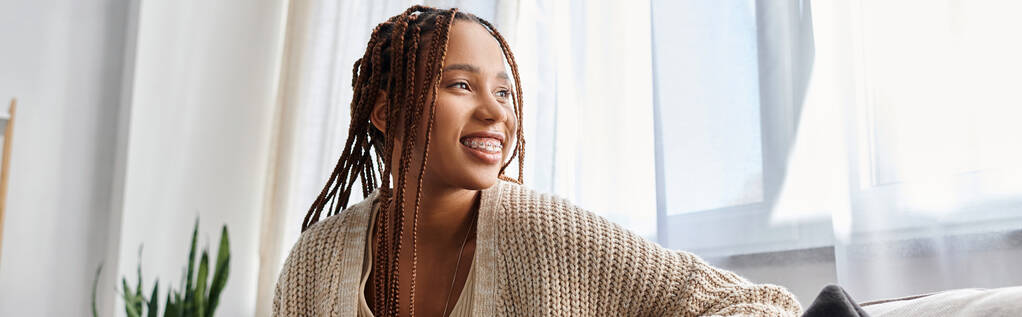 freudig attraktive afrikanisch-amerikanische Frau in Homewear mit Hosenträgern posiert und wegschaut, Banner - Foto, Bild
