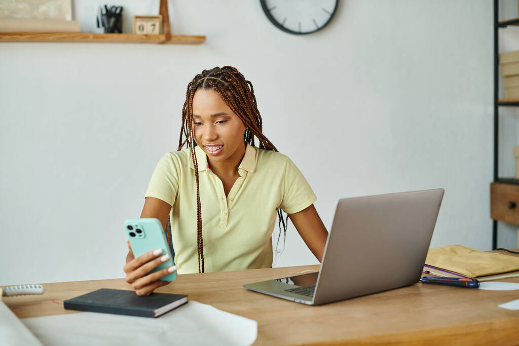 atrakcyjny wesoły afrykański amerykański sprzedawca kobiet patrząc na jej smartfon podczas pracy, dostawy - Zdjęcie, obraz