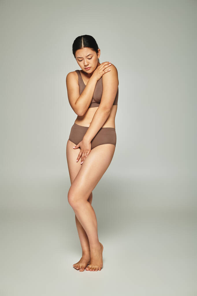 järkyttynyt aasialainen nainen alusvaatteet kattaa kehon samalla syleilee itseään harmaa tausta, kehon häpeä - Valokuva, kuva