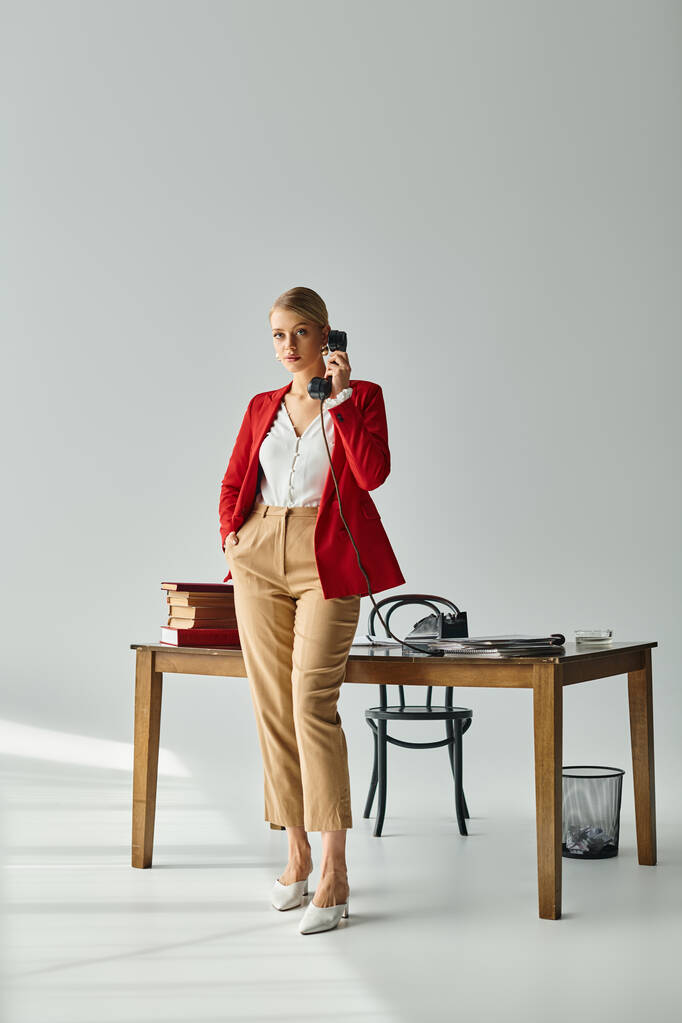 atractiva mujer joven en traje vibrante posando con la mano en el bolsillo mientras habla por teléfono retro - Foto, Imagen