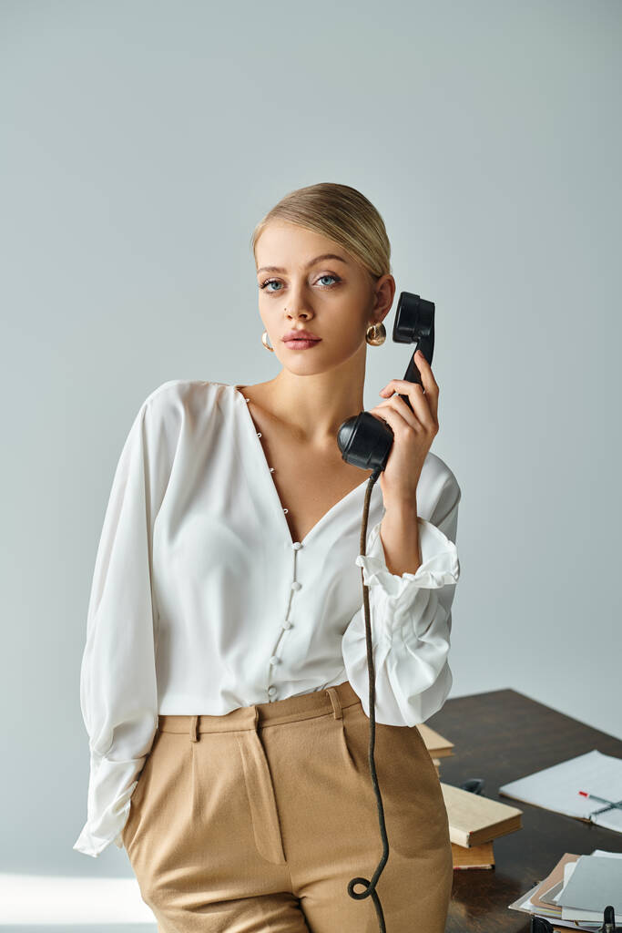 aantrekkelijke jonge vrouw met blond verzameld haar praten door retro telefoon en op zoek naar camera - Foto, afbeelding