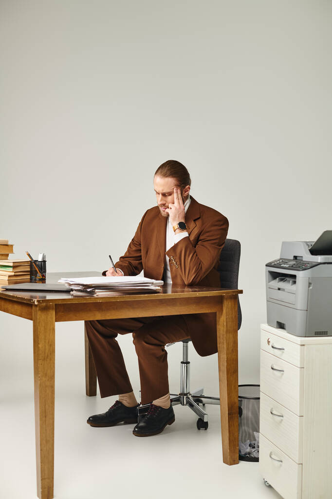трудолюбивый мужчина-модель в элегантной куртке делает заметки, сидя за столом с бумажной работой - Фото, изображение