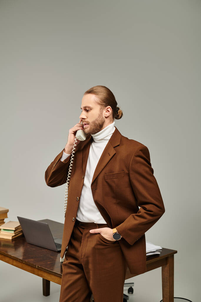 handsome young male model in brown stylish jacket talking by vintage phone with hand in pocket - Photo, Image