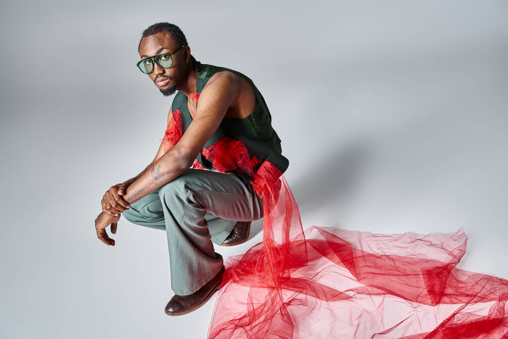 appealing african american man in fashionable attire squatting on gray backdrop, fashion concept - Photo, Image