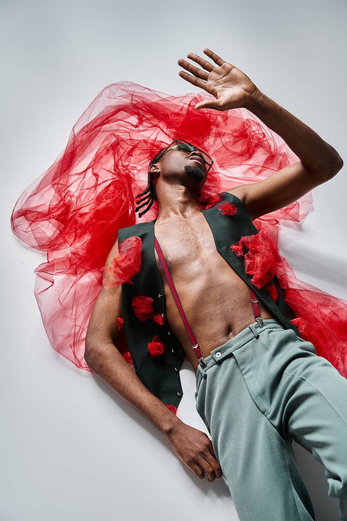 schöner modischer afrikanisch-amerikanischer Mann mit Sonnenbrille im trendigen Outfit auf dem Boden liegend, Mode - Foto, Bild