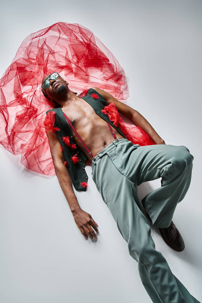 csábító fiatal afro-amerikai férfi modell élénk öltözékben vörös tüll szövet feküdt a padlón - Fotó, kép