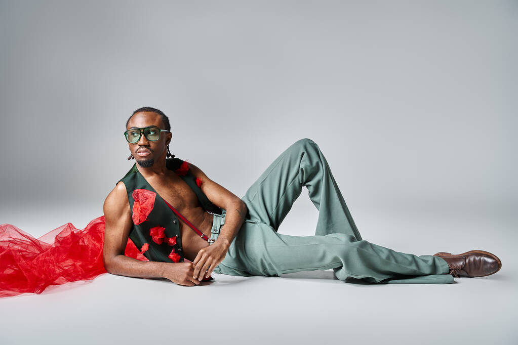 atractivo hombre afroamericano en traje vibrante con tela de tul rojo reclinado en el suelo, la moda - Foto, imagen
