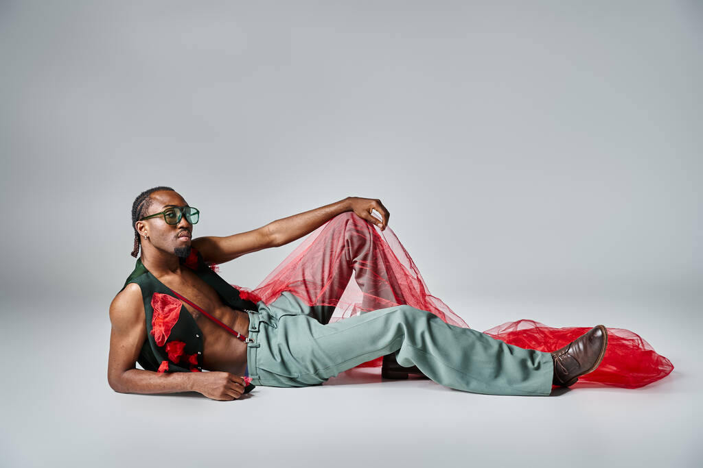 Charmanter afrikanisch-amerikanischer Mann in modischer Kleidung mit rotem Tüll auf dem Boden liegend - Foto, Bild