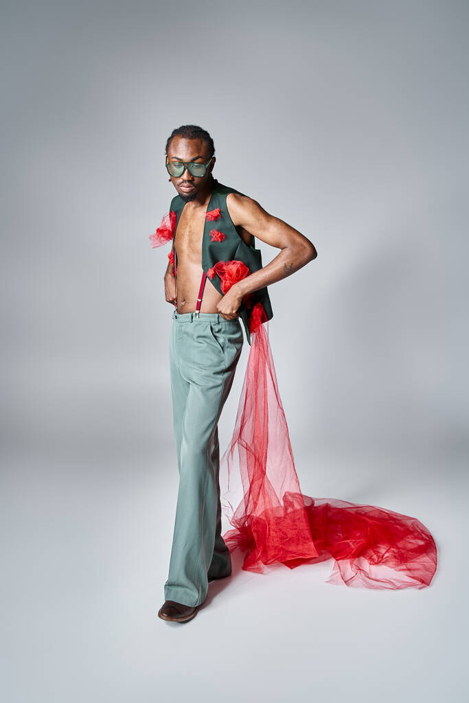 élégant modèle masculin afro-américain avec tissu en tulle rouge posant en mouvement et détournant les yeux - Photo, image
