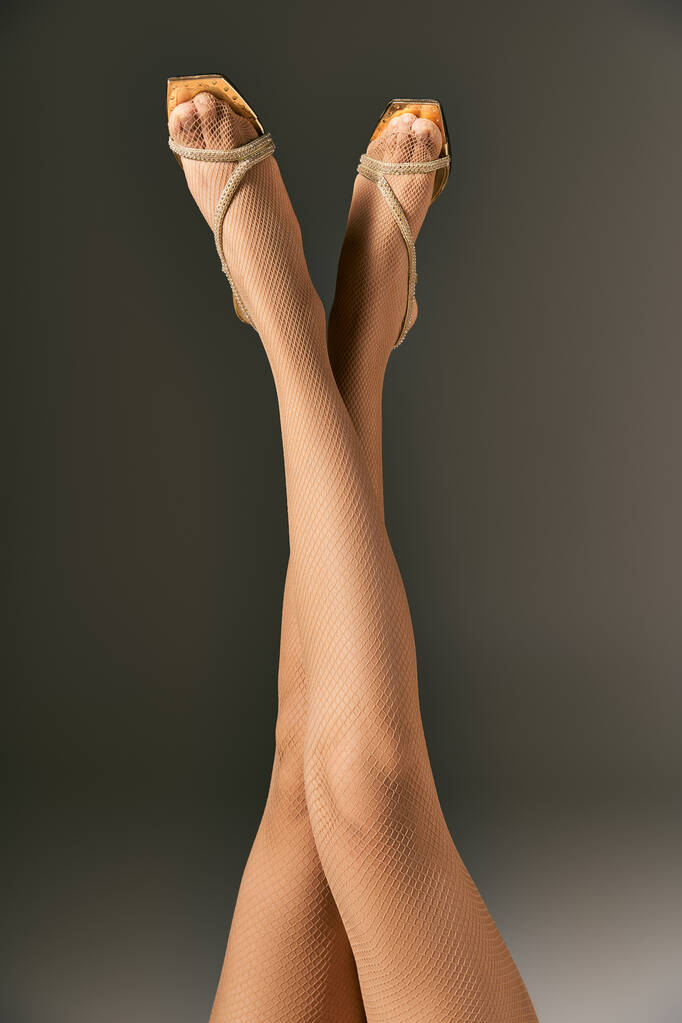 elegantní síťované punčocháče na ženu se zkříženými nohami pózovat ve zlaté obuvi na šedém pozadí - Fotografie, Obrázek