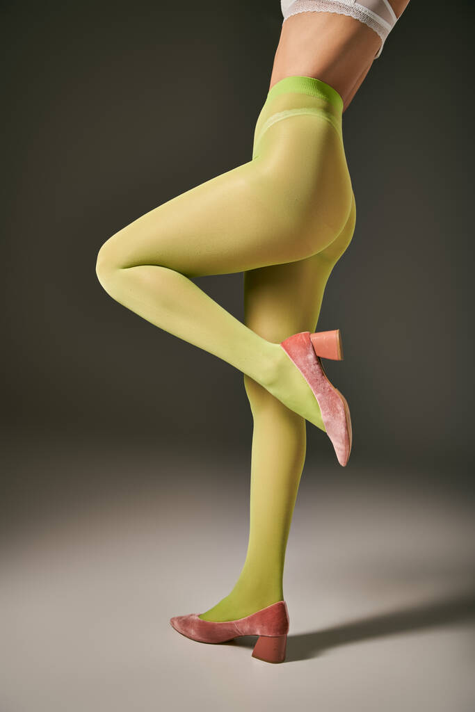 cropped view of young woman in green tights posing in pink shoes on grey background, hosiery - Photo, Image