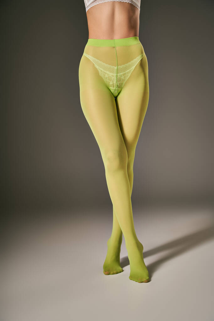 cropped άποψη της νεαρής γυναίκας σε πράσινο νάυλον καλσόν ποζάρουν σε σκούρο γκρι φόντο, σταυρωμένα πόδια - Φωτογραφία, εικόνα
