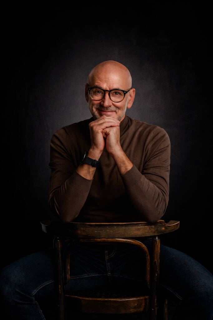 Portrait of mature man with glasses smiling to camera against isolated black background. Confident male wearing turtleneck sweater. - Photo, Image