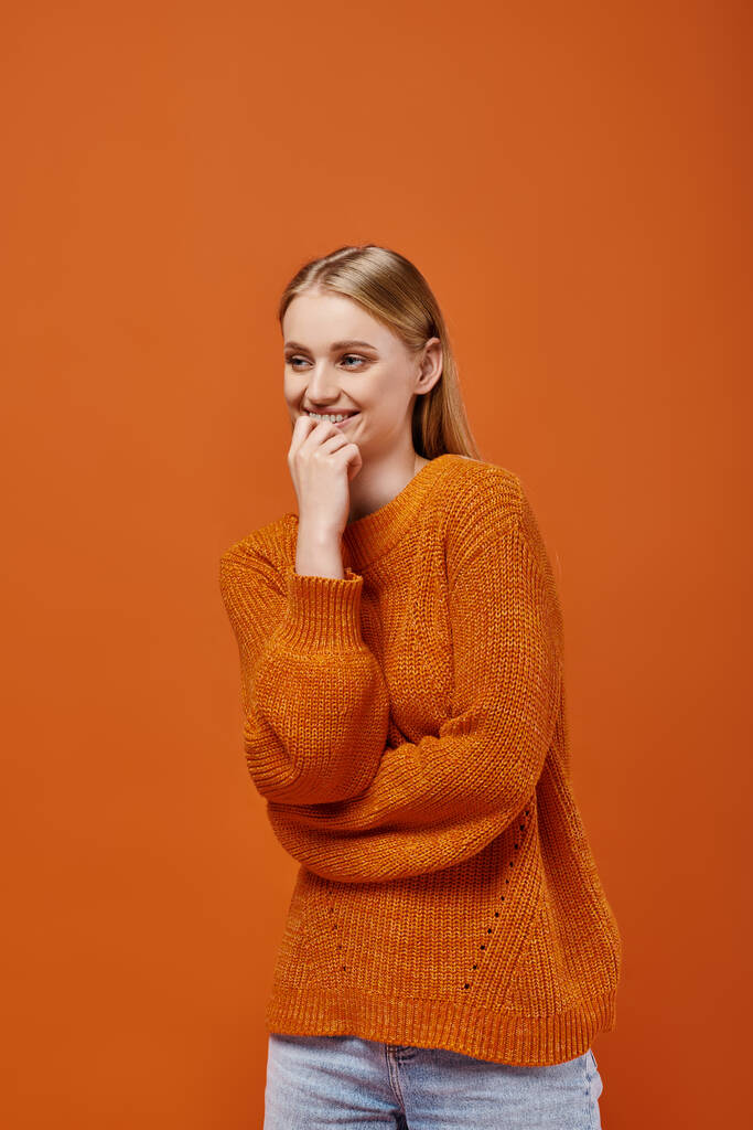 hymyilevä blondi nainen kirkkaassa neulottu villapaita hymyilee ja katselee pois oranssi, talvi tunteita - Valokuva, kuva