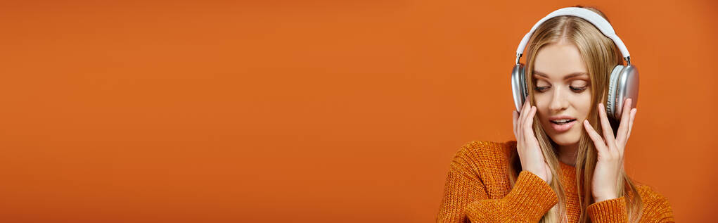 blondi nainen oranssi neulotut pusero ja kuulokkeet kuuntelee musiikkia kirkas tausta, banneri - Valokuva, kuva