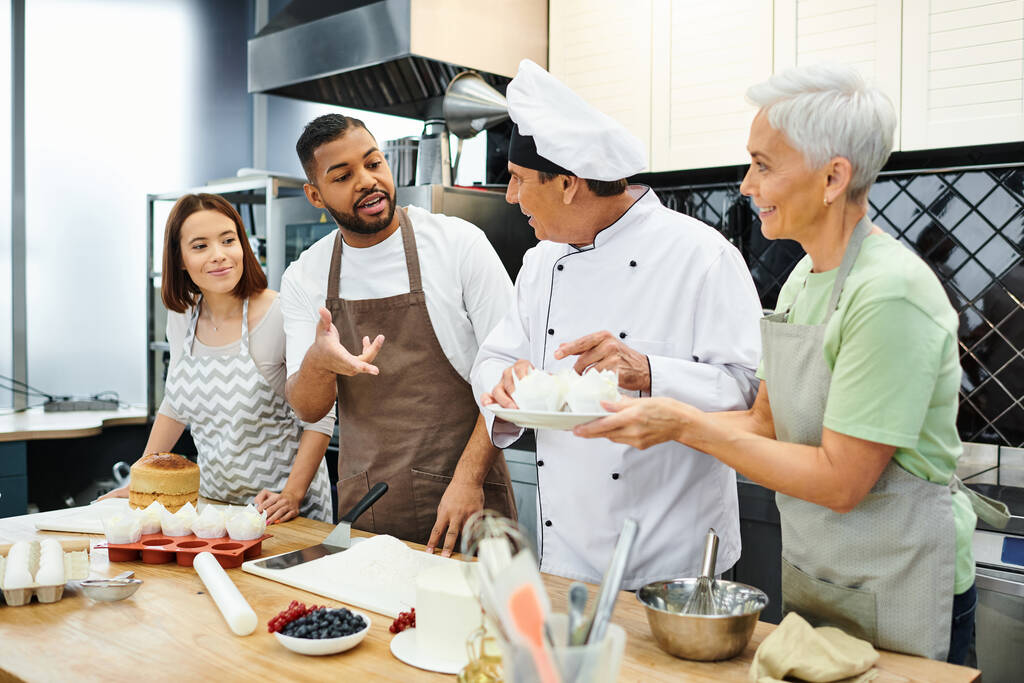 alegres personas multirraciales en delantales hablando con el chef maduro en sombrero blanco, cursos de cocina - Foto, Imagen