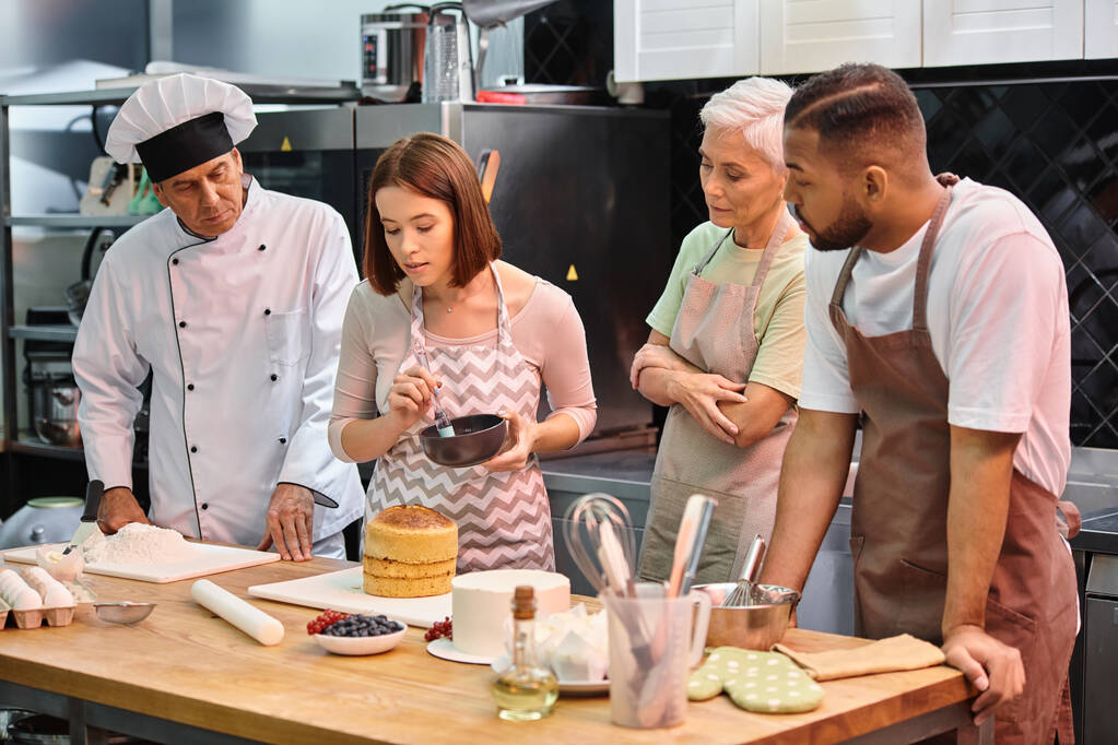 молода приваблива жінка вчиться використовувати силіконову щітку поруч зі своїми різноманітними друзями та шеф-кухарем - Фото, зображення