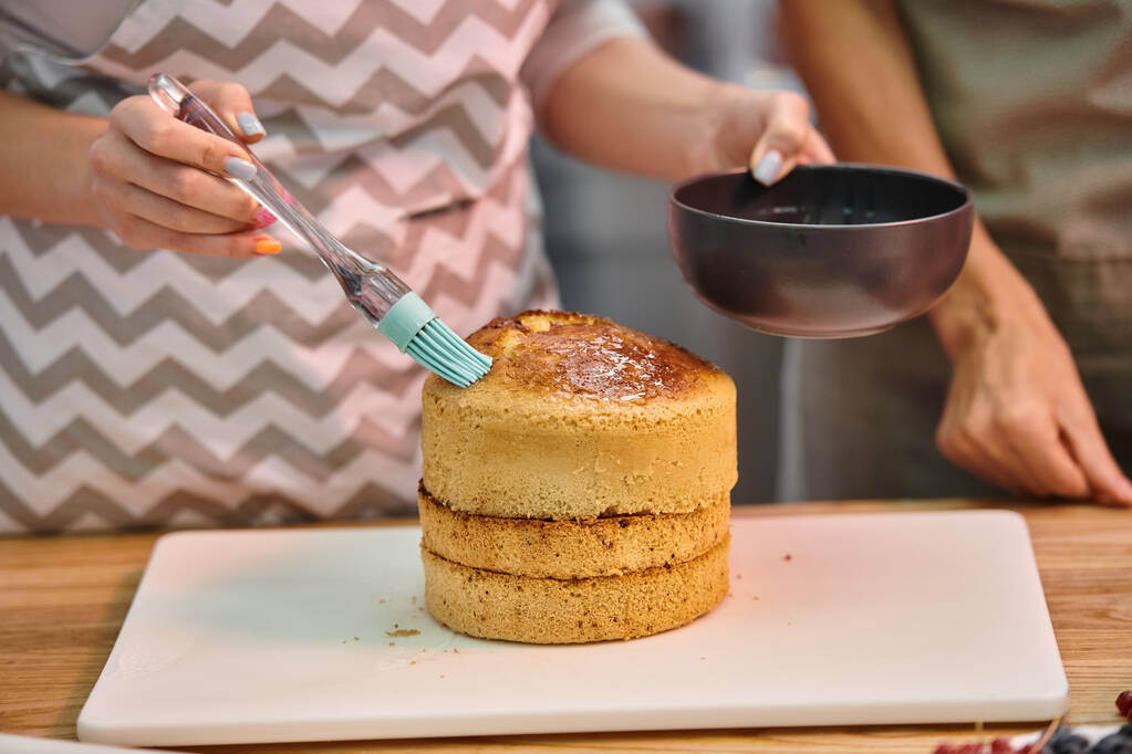 jovem com avental escovando bolo com xarope em delicioso bolo durante a aula de culinária, cursos - Foto, Imagem