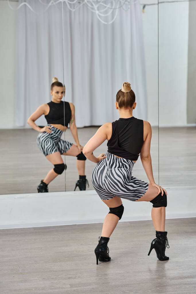 stylische Frau in Zebra-Shorts und schwarzem Top bewegt sich anmutig auf der Tanzfläche und blickt in den Spiegel - Foto, Bild