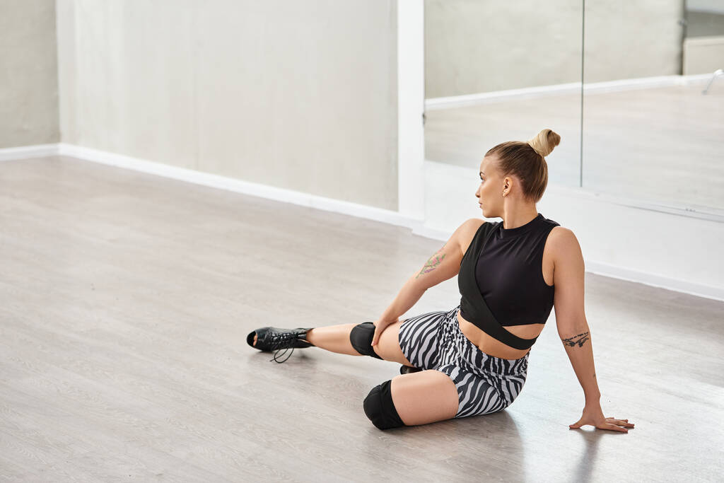 Eine Frau in High Heels balanciert anmutig auf einem Knie, während sie auf der Tanzfläche sitzt - Foto, Bild
