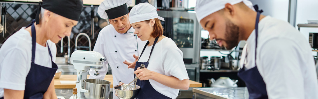volwassen chef-kok in witte hoed praten met zijn hard werkende interraciale koks, zoetwaren, banner - Foto, afbeelding
