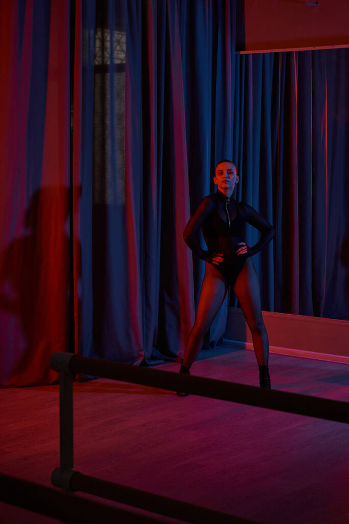 Performerin posiert heftig in ihrem schwarzen Trikot und Netzstrumpfhosen, umrahmt von einem Vorhang - Foto, Bild