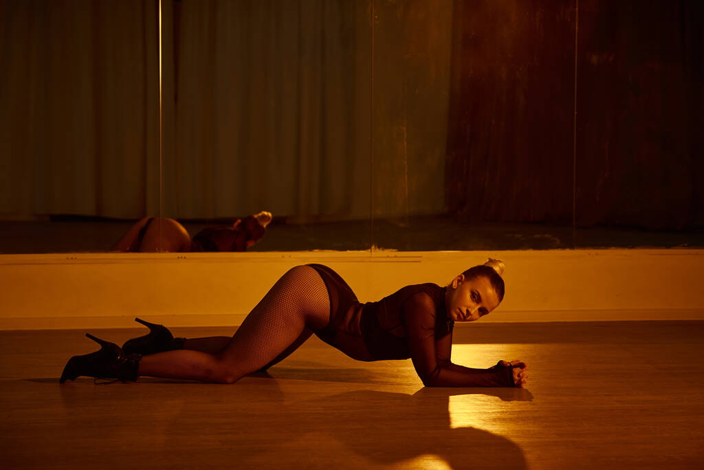 Изящная женщина на высоких каблуках, растягивающая свое тело на полированном полу в танцевальной студии - Фото, изображение