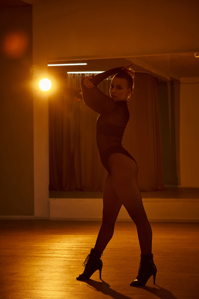 Una bailarina cautivadora en un maillot negro y medias de rejilla se mueve elegantemente contra la pared - Foto, Imagen