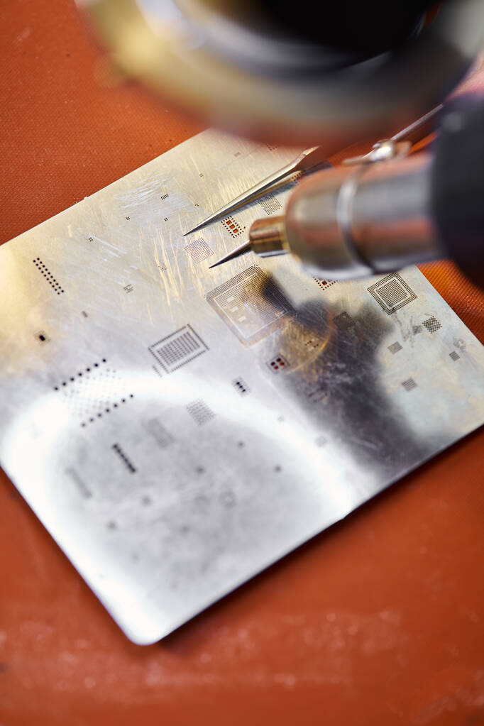close-up zicht op pincet en soldeerbout in de buurt van chipset van elektronisch apparaat in werkplaats - Foto, afbeelding