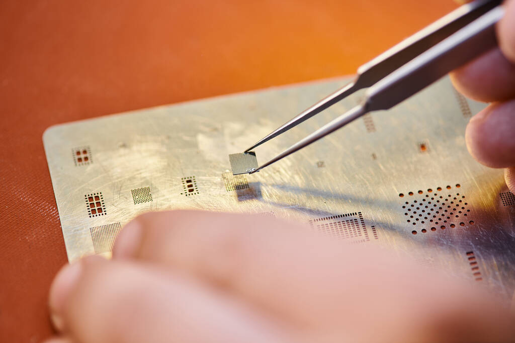 ořezaný pohled zkušeného opraváře s pinzetou a čipem u elektronického obvodu v dílně - Fotografie, Obrázek