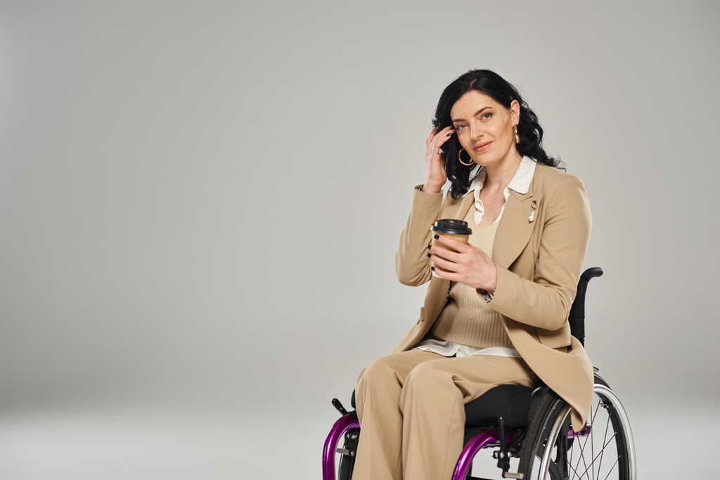 mujer discapacitada de buen aspecto en silla de ruedas en pastel elegante atuendo sosteniendo café, discapacidad - Foto, imagen