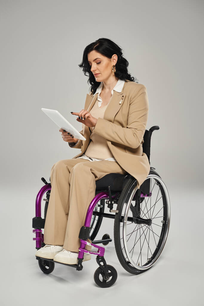 Tekerlekli sandalyede oturan ve tabletine bakan zarif görünümlü engelli bir kadın. - Fotoğraf, Görsel