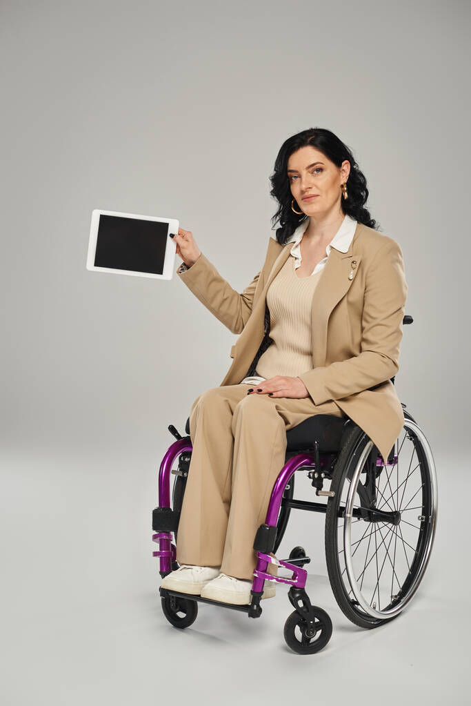 atrakcyjna kobieta z niepełnosprawnością ruchową na wózku inwalidzkim tabletki i patrząc w aparat fotograficzny - Zdjęcie, obraz