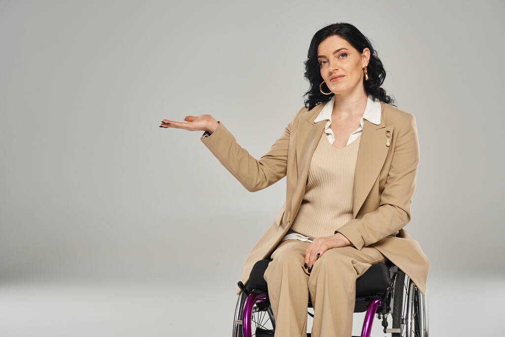 gut aussehende Frau mit Behinderung im Rollstuhl im pastellfarbenen Anzug gestikuliert und blickt in die Kamera - Foto, Bild