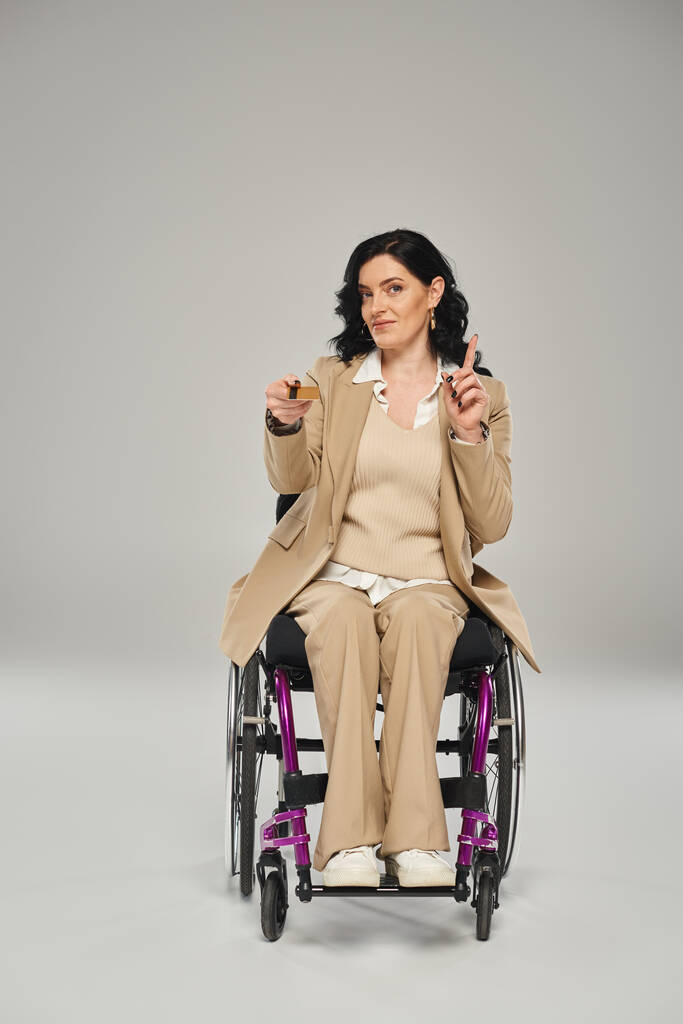 aantrekkelijke gehandicapte vrouw zit in haar rolstoel met credit card en gebaren actief - Foto, afbeelding