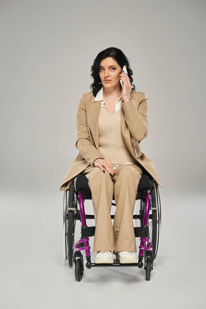 ελκυστική γυναίκα με αναπηρία, με ευφυΐα στην αναπηρική καρέκλα της και μιλώντας στο τηλέφωνο, κοιτάζοντας την κάμερα - Φωτογραφία, εικόνα