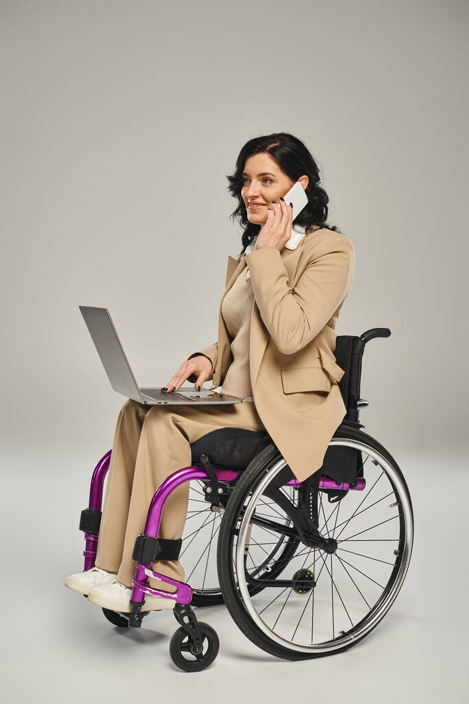 wesoła kobieta z niepełnosprawnością ruchową na wózku inwalidzkim z laptopem i rozmowy telefonicznej - Zdjęcie, obraz