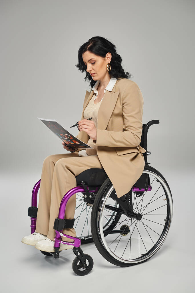 niepełnosprawna pewna siebie kobieta w eleganckim stroju siedzi na wózku inwalidzkim i pracuje nad jej grafiką - Zdjęcie, obraz