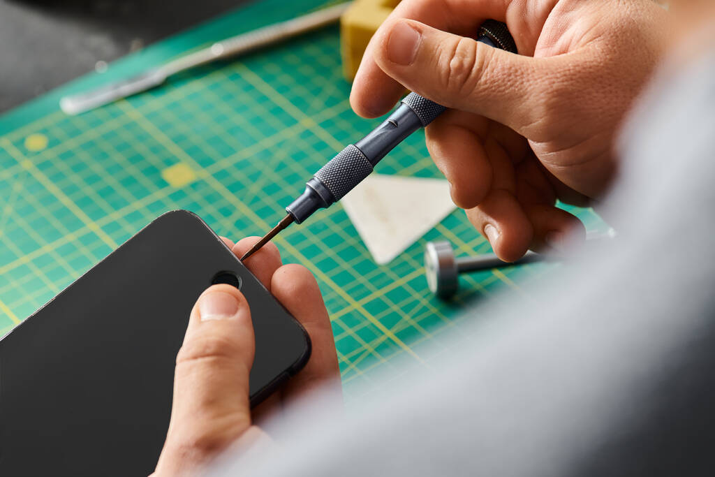 Fachmann öffnet Smartphone mit Schraubenzieher in moderner Reparaturwerkstatt - Foto, Bild