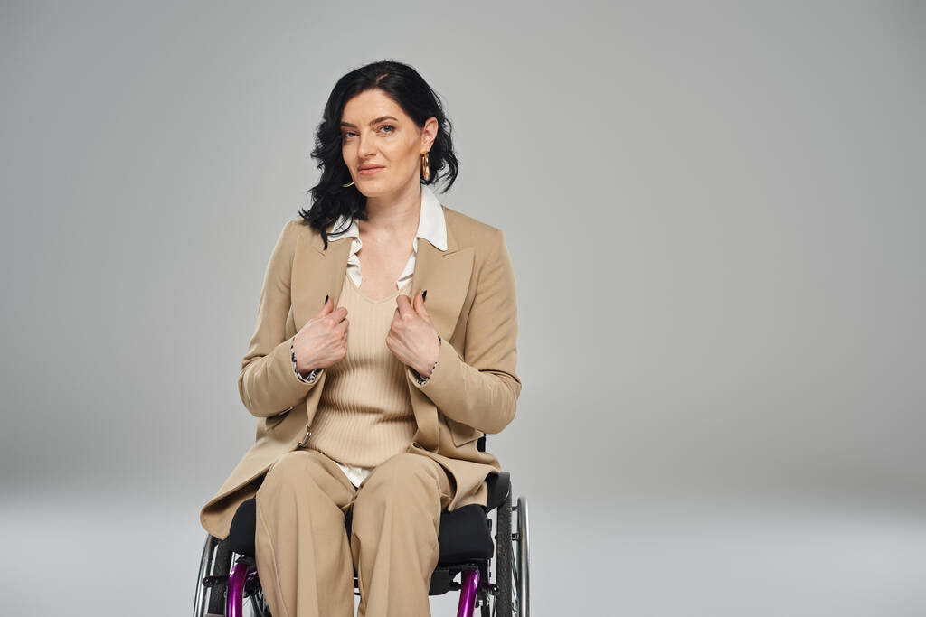 donna sicura di sé con disabilità in abito elegante pastello seduto sulla sedia a rotelle e guardando la fotocamera - Foto, immagini