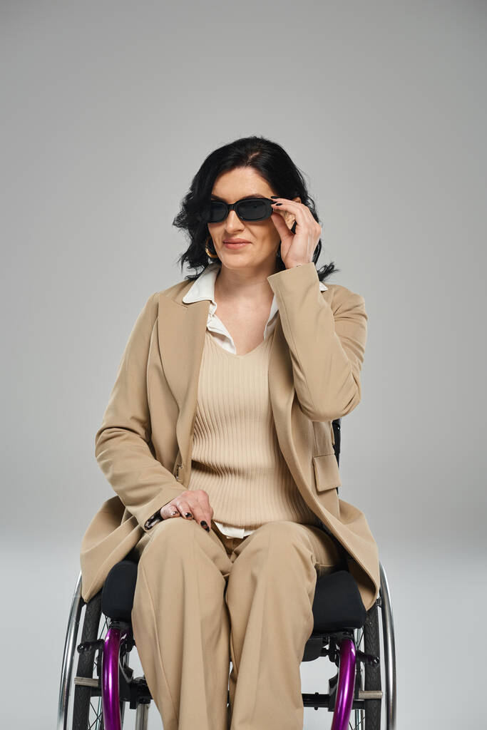 allegra bella donna con disabilità in sedia a rotelle indossando occhiali da sole e guardando la fotocamera - Foto, immagini