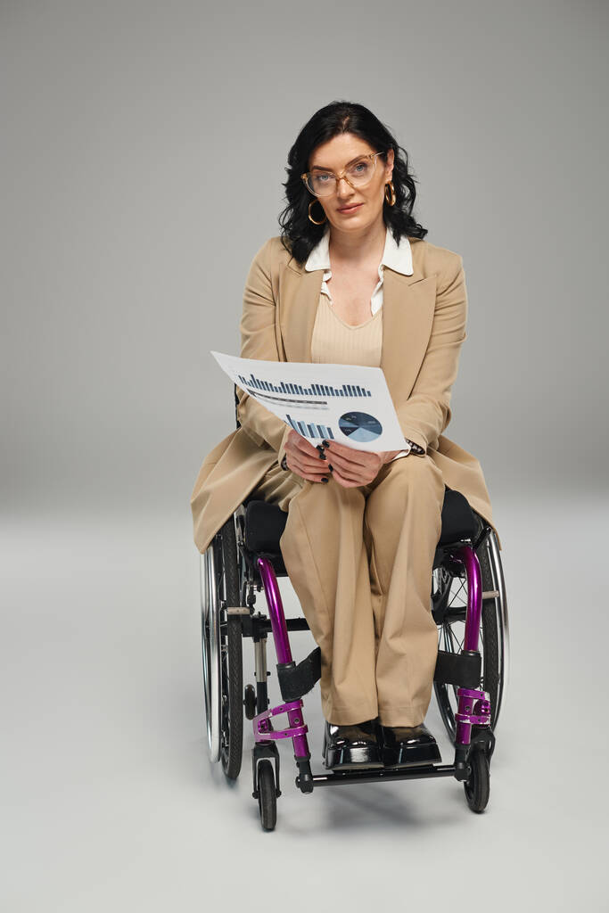focalizzata donna disabile con occhiali e capelli ondulati nella sua sedia a rotelle con grafica guardando la fotocamera - Foto, immagini